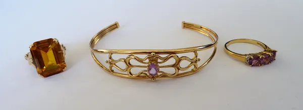 A gold ring, claw set with a cut cornered rectangular step cut citrine, a gold ring, mounted with a row of three cushion shaped amethysts, between dia