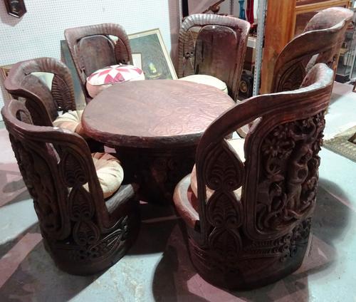 A 20th century African carved hardwood dining table, 135cm wide and six matching chairs with slab seats and leather cushions, (7).    BAY 1