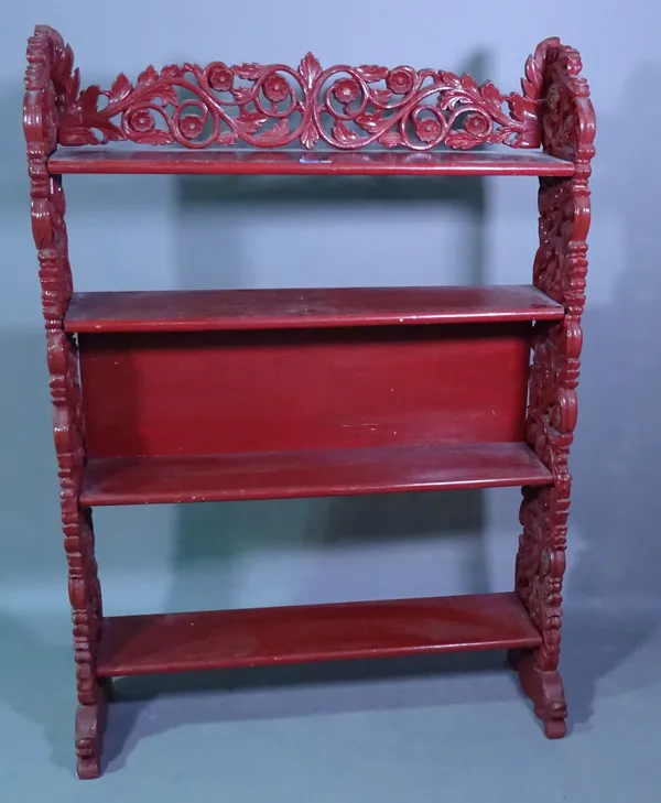 An early 20th century Chinese red painted four tier open bookcase with carved supports, 98cm wide x 139cm high.   G9