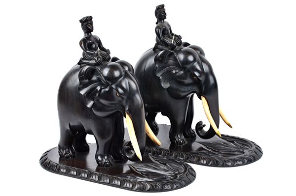 A pair of Indian carved ebony elephants, late 19th/early 20th century, each mounted with a figure over a foliate carved and shaped base, 36cm high, (2