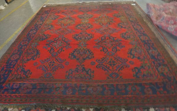 A Turkey carpet, the red field with three columns of stylised medallions, an indigo rosette and leaf spray border, 350cm x 308cm.