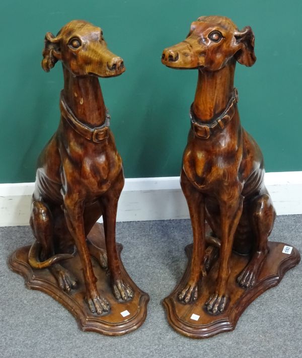 A pair of 20th century carved wood figures modelled as seated greyhounds on shaped bases, 77cm high. (2)