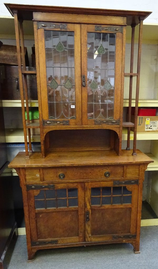 An early 20th century oak Arts and Crafts display cabinet cupboard, the pair of leaded glass doors over single drawer and further cupboards, on steppe