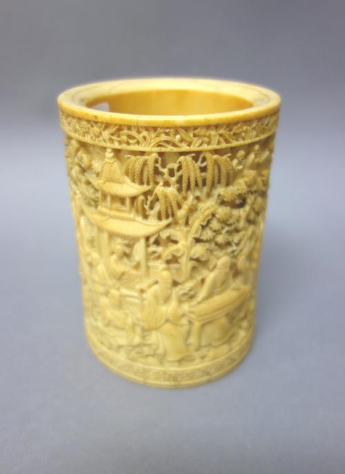 A Chinese ivory brush pot, late 19th century, of cylindrical form, profusely carved with scholars, pavilions, rocks and bamboo, (base plate lacking),