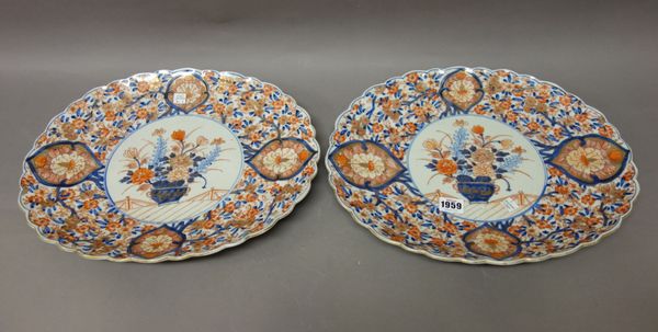 A pair of Japanese Imari oval fluted dishes, Meiji period, each painted in the centre with a vase of flowers, on a ground filled with flowering branch