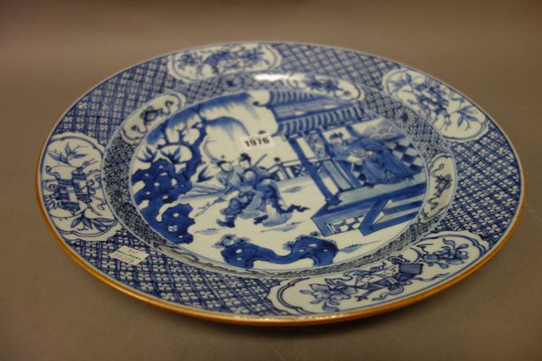 A Chinese blue and white dish, Kangxi, painted with a figure on a terrace waving goodbye to a young man and woman, beneath a diaper pattern border res