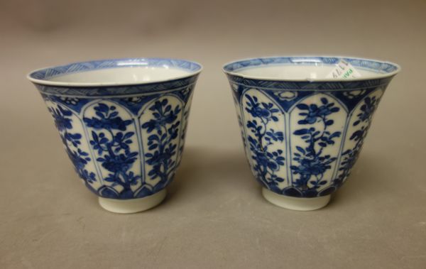 A pair of Chinese blue and white porcelain beakers, Kangxi, painted with panels of flowering plants, (a.f); also a pair of similar saucers; a pair of