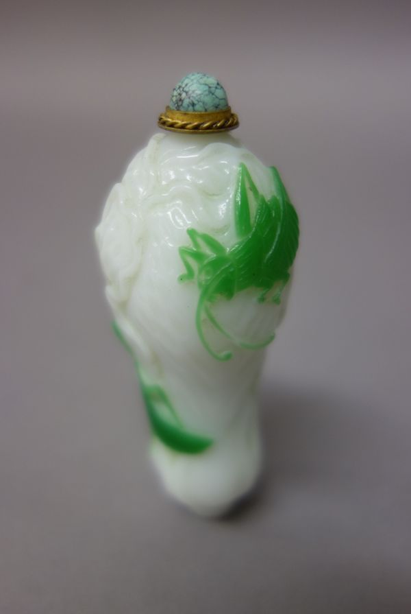 A Chinese green overlay white glass snuff bottle, 20th century, carved with two grasshoppers clambering up the leaves of a pak choi, 7cm. high; also a