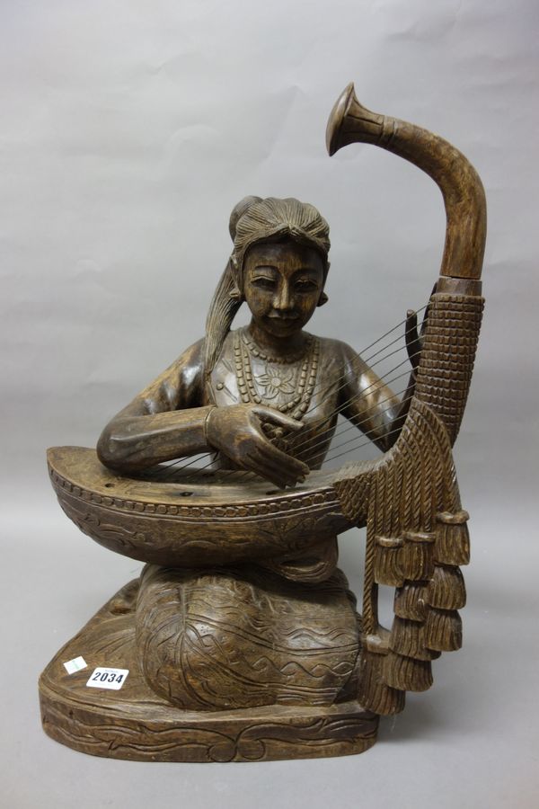 A Burmese wood figure of a musician, 20th century, carved as a seated young woman playing the harp, 53cm. high.