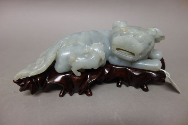 A Chinese greyish-celadon jade lion group, 19th century, carved with a recumbent lion with incised mane and long tail, its head turned to the right to