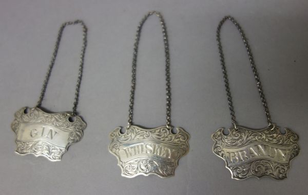 A pair of Victorian silver decanter labels, each of cartouche shaped form, detailed Brandy and Gin, by George Unite, Birmingham 1845 and another later