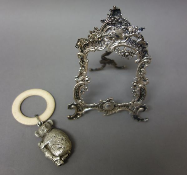 A silver photograph frame of cartouche shaped form, in the Rococo style, having cherub and floral motifs, import mark London 1895, a silver rattle for