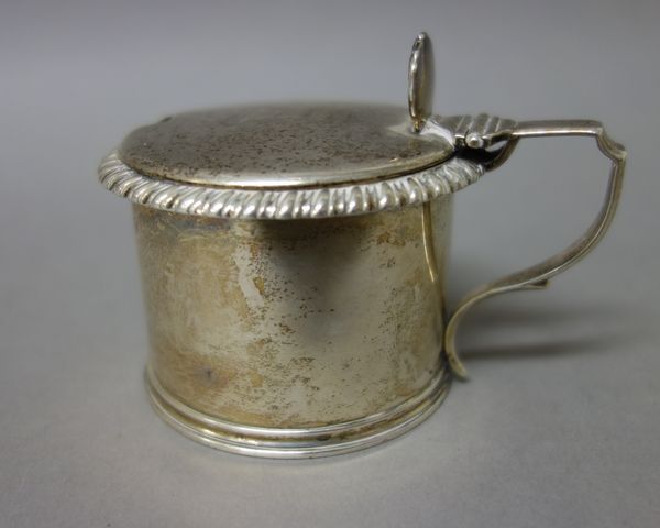 A William IV silver hinge lidded mustard pot of cylindrical form, decorated with a gadrooned rim, crest engraved, London 1834, with a blue glass liner