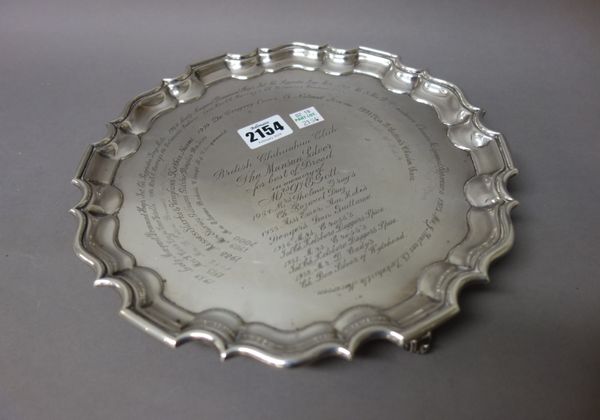 A silver salver of shaped circular form, having a pie crust rim raised on three scrolled feet, diameter 25.5 cm, London 1898 and a plated cake dish of