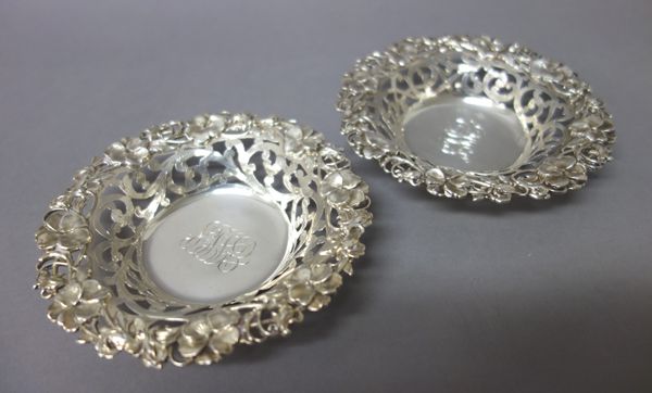 A pair of Sterling bonbon dishes, each with scroll pierced decoration within a floral moulded rim, monogram engraved to the centre, a Victorian silver