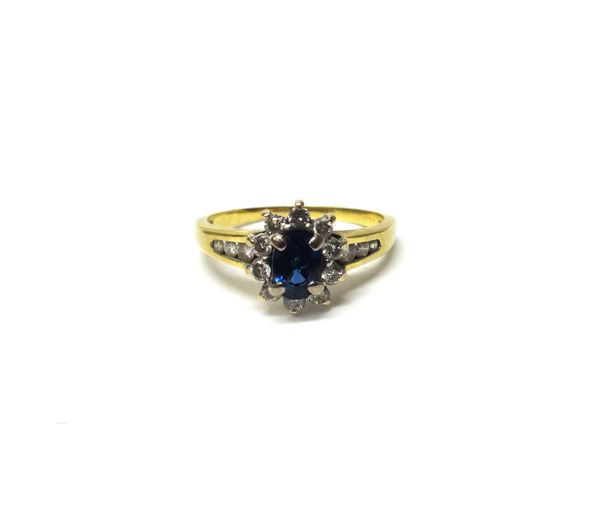 An 18 ct gold, sapphire and diamond set oval cluster ring, claw set with the oval cut sapphire in a surround of circular cut diamonds, between diamond