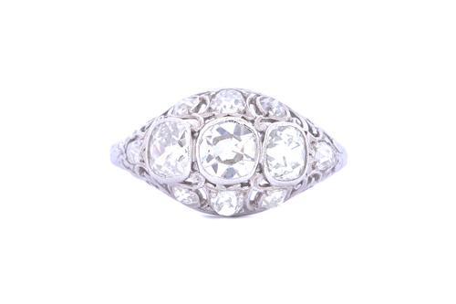 A white gold and diamond ring, collet set with the three principle cushion shaped diamonds to the centre, within a pierced openwork surround, further