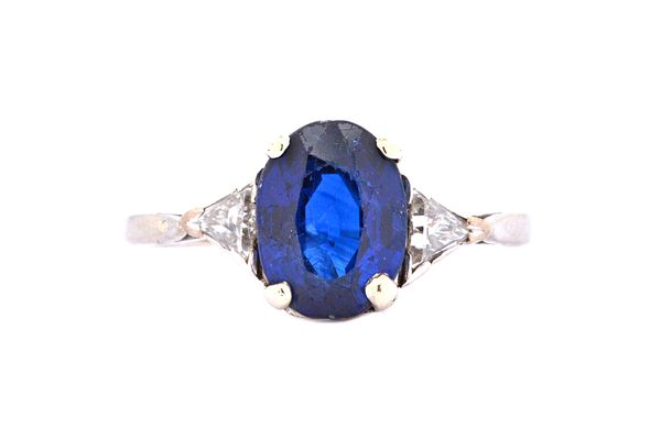 A sapphire and diamond three stone ring, claw set with the oval cut sapphire between two triangular cut diamonds, estimated weight of the sapphire app