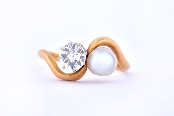 A gold, diamond and cultured pearl set ring, claw set with a cushion shaped diamond and with a cultured pearl, in a crossover design, ring size L and