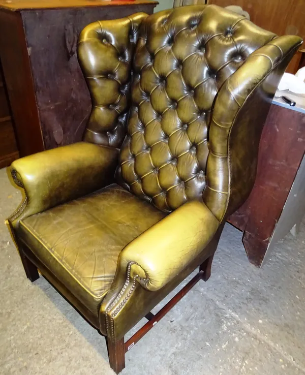 A 20th century mahogany framed wingback armchair with green leather button back upholstery on square block supports.  Dis
