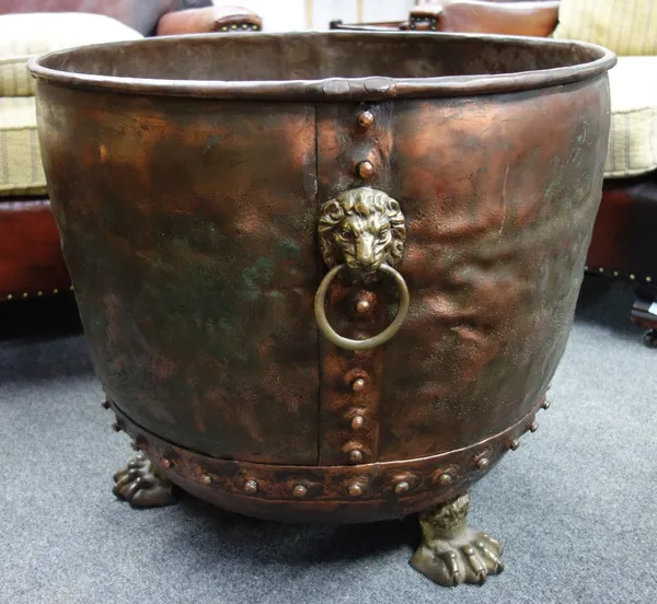 A copper log bin, late 19th century, of circular riveted form flanked by twin brass lion mask ring handles on three brass lion paw feet, (63cm diamete