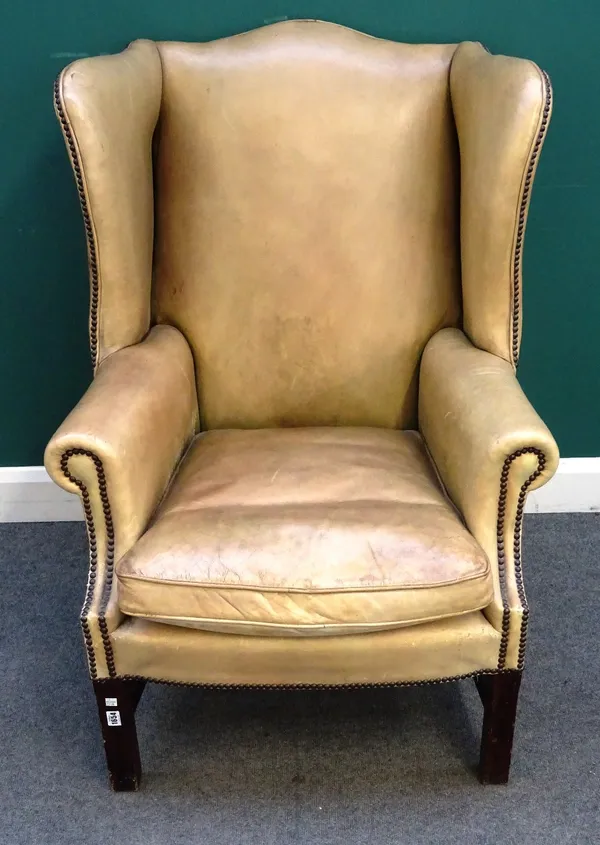 A George II style wing armchair, with studded light tan leather upholstery, on mahogany block supports, 80cm wide x 110cm high.