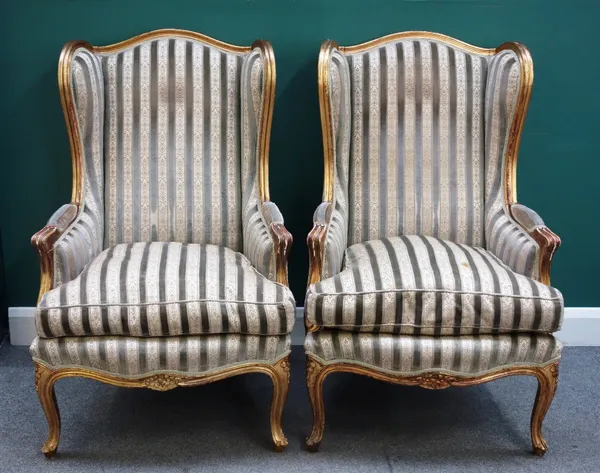 A pair of Louis XV style gilt framed wing back armchairs, with arched crest rail and bow seat, on squat cabriole supports, each 71cm wide x 113cm high