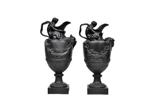 A pair of Wedgwood black basalt 'wine' and 'water' ewers, late 19th century, with figural handles and applied masks, over a fluted socle and square ba