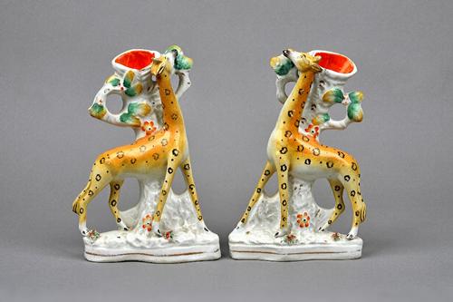 A rare pair of Staffordshire pottery spill vases, mid 19th century, each modelled as a giraffe standing against a tree with head raised towards the le