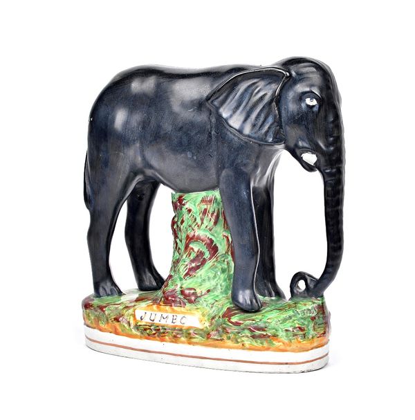 A Staffordshire pottery figure of `Jumbo', circa 1885, the black elephant modelled standing four-square, supported on a grassy mound, on an oval title