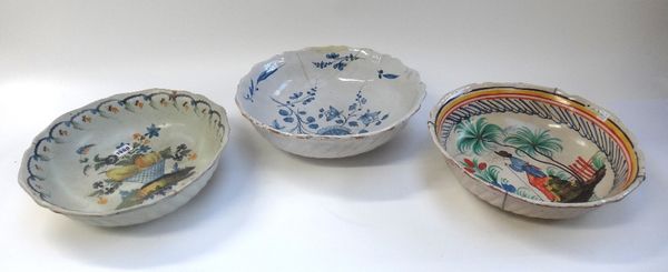 A French faience bowl, early 19th century, hand painted with a bowl of still life fruit, 35cm diam., and two further later faience bowls, (a.f) (3).