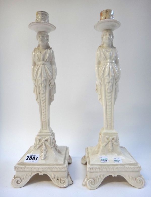 A near pair of creamware pottery candlesticks, 20th century, each modelled as a robed classical female over a square base and four scroll feet, 40cm h