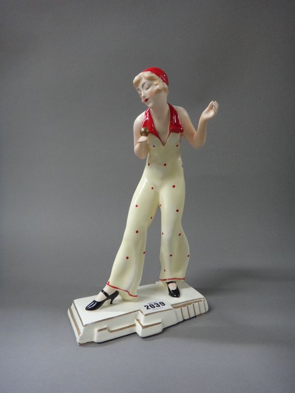 A Royal Dux Art Deco figurine, 'Balance', by Schaff, circa 1930, modelled in a red spotted yellow trouser suit and cap, supporting a gold ball on her