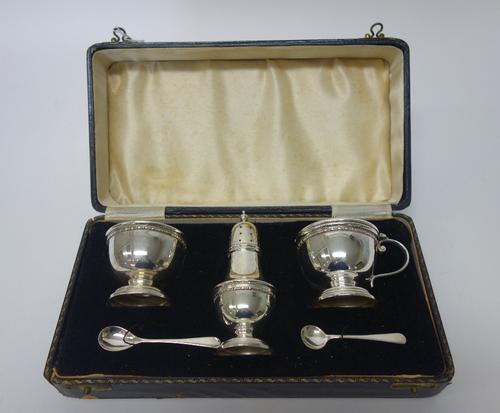 A silver three piece condiment set, comprising; a mustard pot, a salt and a pepperette and two condiment spoons, Birmingham 1934, combined weight 178