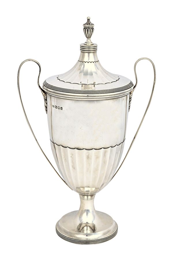 A silver twin handled trophy cup and cover, of Adam style, with partly fluted decoration within reeded bands and with a fluted urn shaped finial, Lond