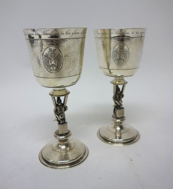 Two similar silver goblets, made for The Worshipful Company of Blacksmiths, each engraved with a coat of arms, a model of a blacksmith at work to the