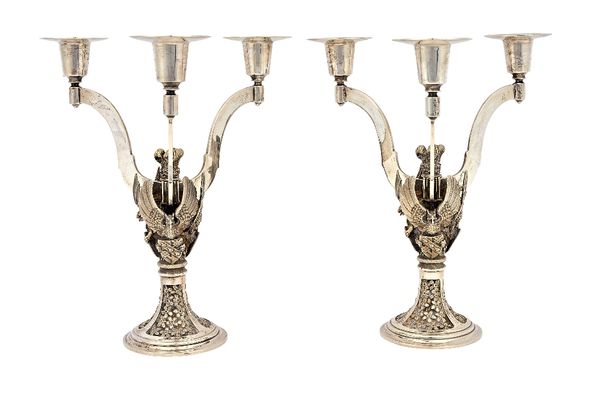 A pair of silver triple light table candelabra, each decorated with three birds and mythological animals in flight, each holding a shield, raised on a