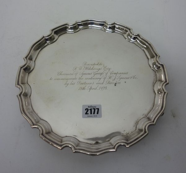 A silver salver, of shaped circular form, decorated with a pie-crust rim, in the Chippendale style, raised on three scrolling feet, presentation inscr