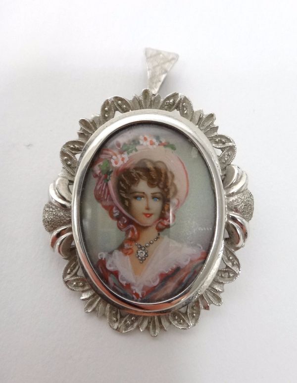 A white gold oval pendant brooch, the centre glazed with the portrait of a lady wearing a hat with flowers, the mount decorated with a pierced border,