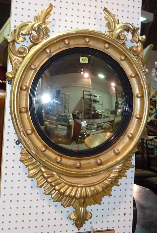 A Regency style gilt framed circular convex wall mirror, with ebonised slip and gadrooned carved lower frieze, 58cm wide x 90cm high.  ROST