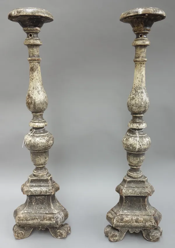 A pair of Italian grey painted carved wooden altar candlesticks, each of turned form, on a triform base and three scroll feet (a.f), 75cm high, (2).