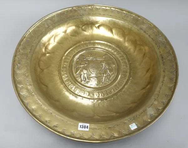 A brass alms dish, 17th century, embossed with two men gathering harvest, with a wide text border and foliate surround, 58cm diameter.