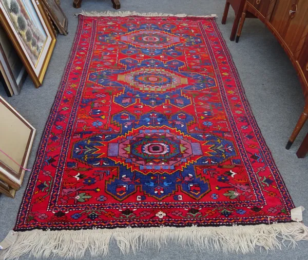 A Caucasian rug of Kazak design, the madder field with three bold indigo medallions, supporting flowers; a complementary madder border, 247cm x 148cm.
