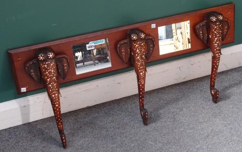 A set of three early 20th century Indian bone inlaid elephant head coat hooks, mounted on a mirrored backboard, 102cm wide x 47cm high.