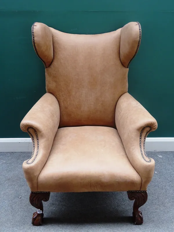 An 18th century style brown leather upholstered wingback chair, of unusual outline, on mahogany claw and ball feet, 85cm wide x 119cm high.