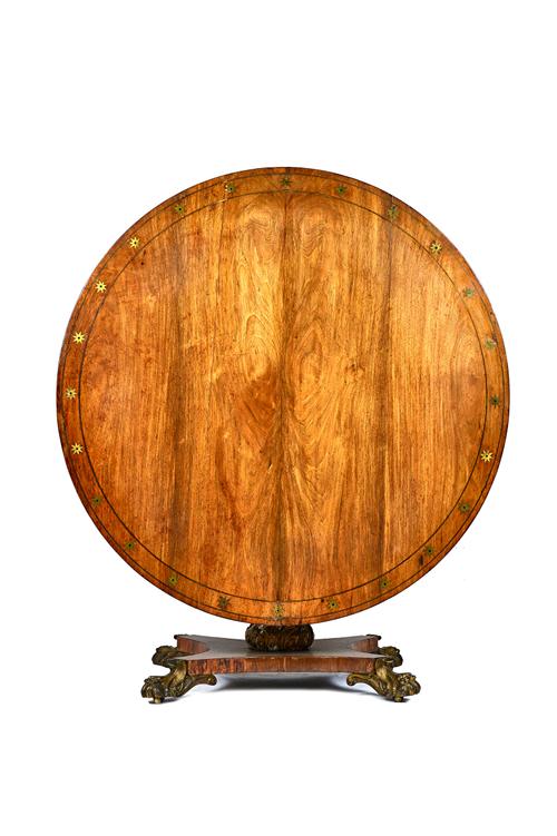 A William IV brass inlaid mahogany centre table, the circular snap top on turned column and quatrefoil platform, resting on four gilt bronze lion's pa