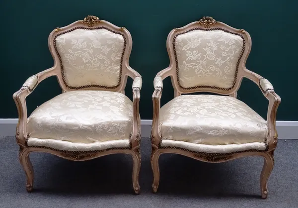 A pair of Louis XV style cream painted parcel gilt open armchairs, each with serpentine seat on scroll supports, 67cm wide x 93cm high (2).