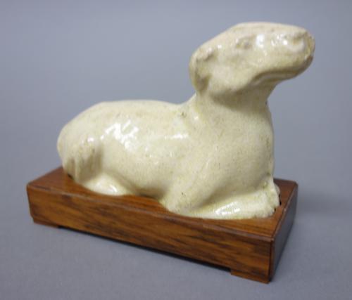 A Chinese straw glazed pottery model of a recumbent dog, probably Tang dynasty, the animal looking straight ahead, 10cm. length, later wood stand.Prov