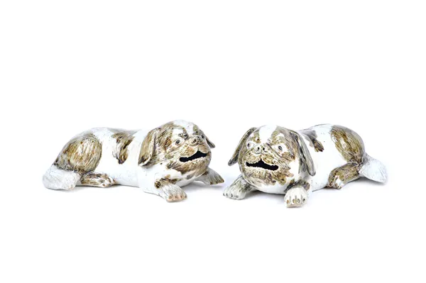 A pair of Chinese export biscuit glazed recumbent dogs, early 19th century, each with one foreleg extended, the wide head with open mouth and floppy e