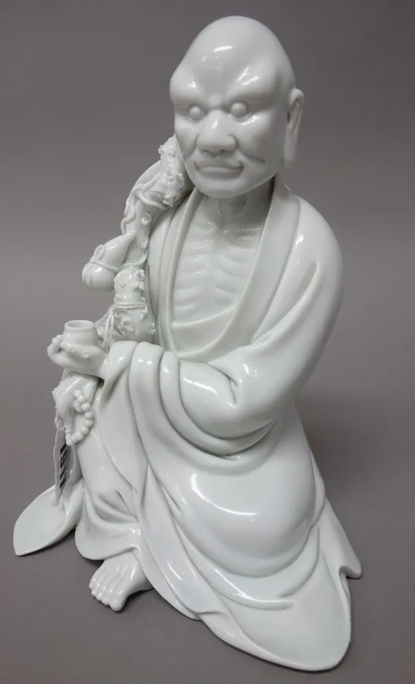 A Chinese blanc-de-chine figure of Li Tieguai, probably early 20th century, seated holding a bowl and rosary, hugging a staff suspended with a gourd f